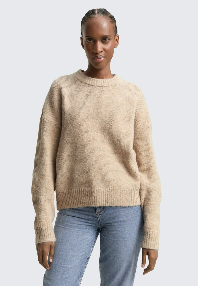 Beige gebreide trui met een gestructureerde afwerking, geribbelde mouwen en een ronde hals. Gecombineerd met lichtblauwe denim jeans. Eenvoudig, casual ontwerp.