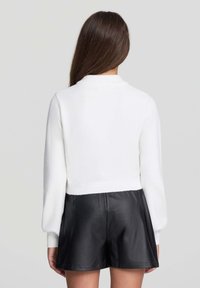 Krótkie białe sweter z wysokim kołnierzem i prążkowanym wykończeniem. Połączony z czarnymi skórzanymi szortami. Gładka tekstura, długie rękawy.