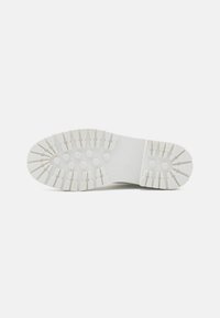 Biała podeszwa sneakersów z widocznymi wzorami bieżnika, heksagonalnymi rowkami, teksturowanymi wypustkami oraz płaskim kształtem dla lepszej przyczepności i wsparcia.