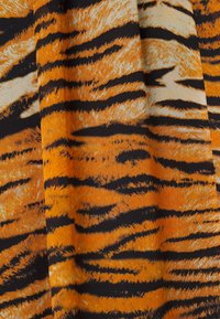 Tissu orange et noir avec un motif à rayures de tigre, présentant des plis et la texture du matériau.
