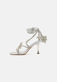 Sandale à talons hauts en argent avec de délicates accents de fleurs en cristal, deux brides et une finition métallique élégante. Design ouvert avec un talon fin.