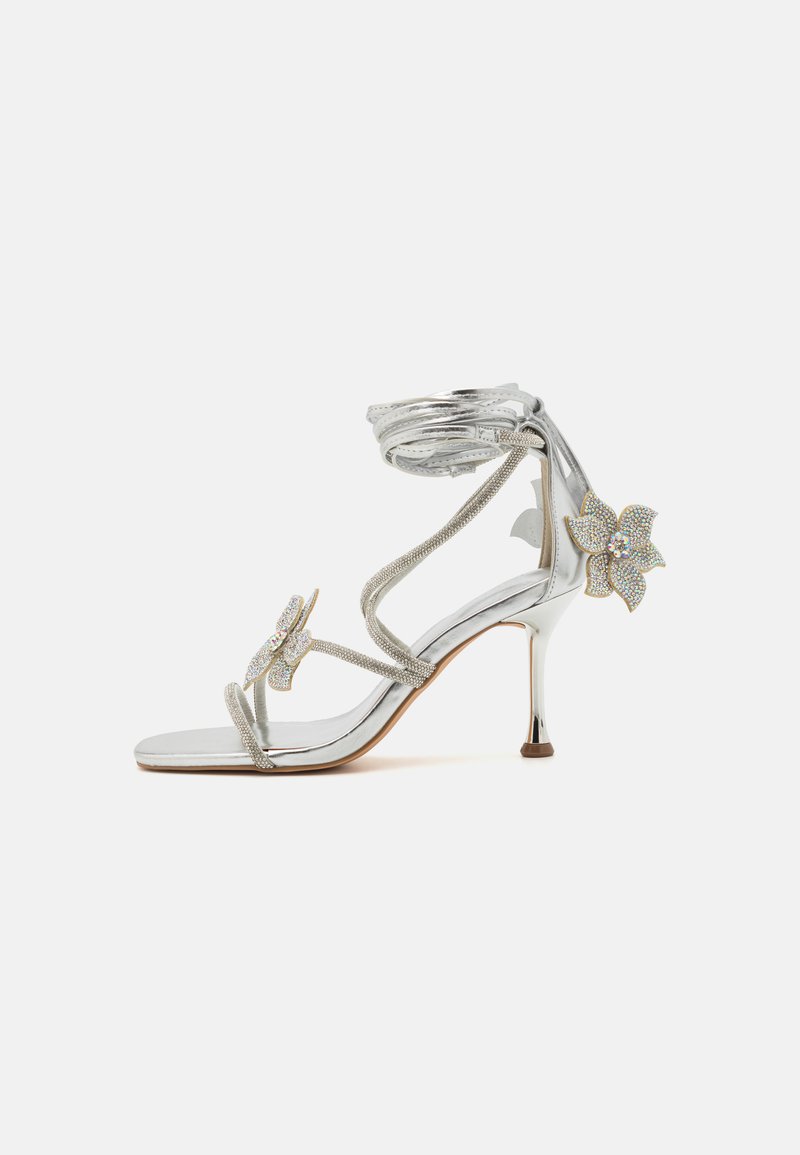 Sandale à talons hauts en argent avec de délicates accents de fleurs en cristal, deux brides et une finition métallique élégante. Design ouvert avec un talon fin.