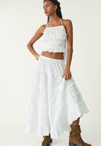 Biely dvojdielny outfit pozostávajúci z volánového crop topu s tenkými ramienkami a dlhých, poschodových sukýň; vyrobený z ľahkého materiálu.