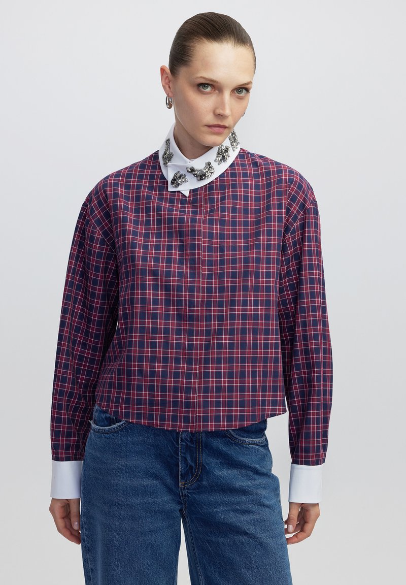 Camicia a quadri rossa e blu con colletto bianco decorato con accenti metallici; presenta maniche lunghe e un design a vestibilità rilassata.