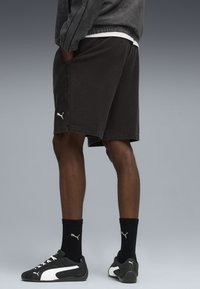 Sorte bomulds shorts med sidelommer, prydet med et hvidt Puma-logo. Båret med sorte sokker og sneakers, hvilket skaber et afslappet look.