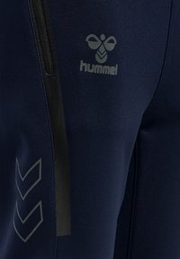 Navy Sporthose mit schlanker Passform, ausgestattet mit einer schwarzen Reißverschlusstasche, grauer Markenveredelung und Akzenten in Chevron-Muster an der unteren Beinpartie.
