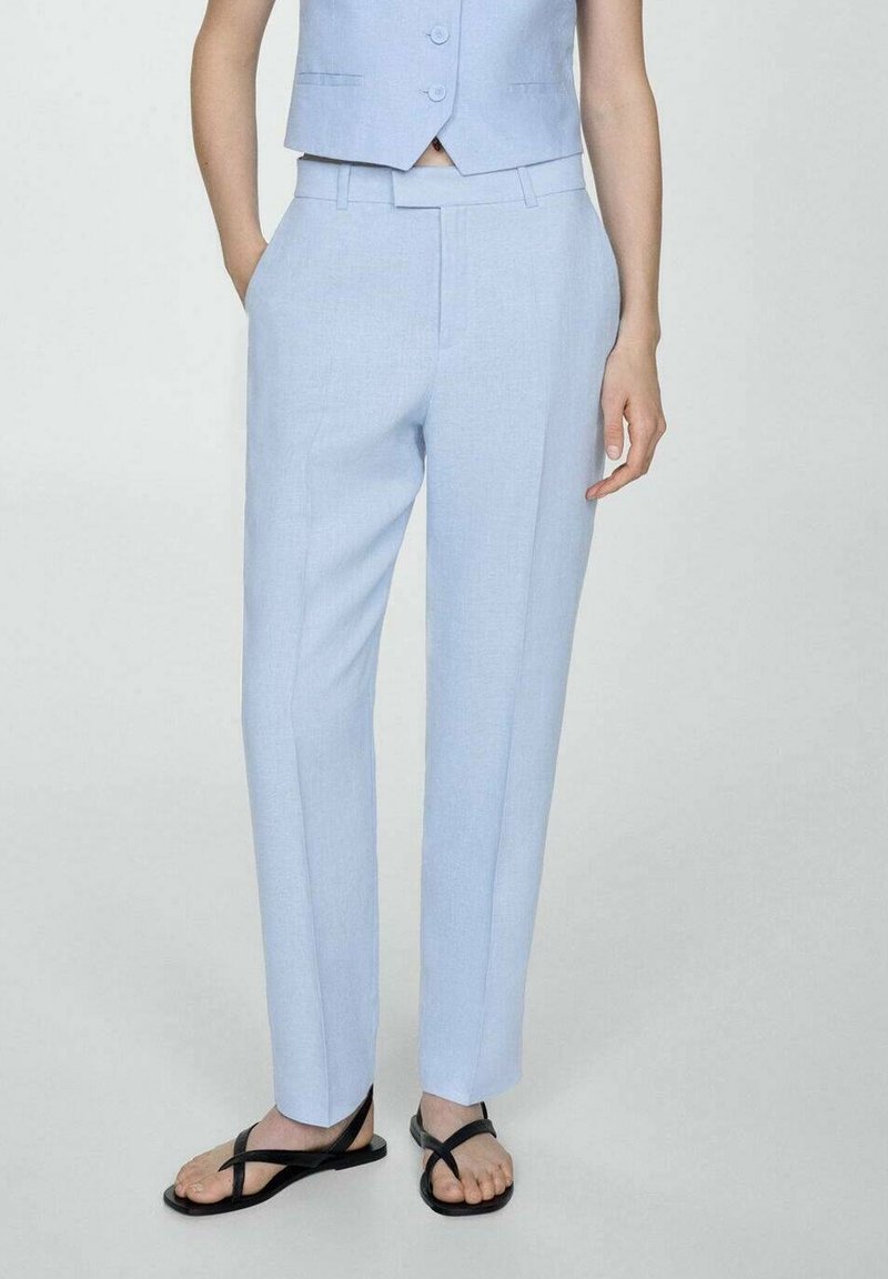 Pantalon bleu clair sur mesure en tissu texturé, avec une coupe droite, des poches latérales et une taille mi-haute. Associé à des tongs noires.