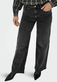 Črne široke kavbojke z visokim pasom in sprednjimi žepi, ki imajo zbledel videz, šivano dekoracijo in srebrno gumbno zapiranje.