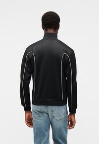 Μαύρο φούτερ με ψηλό γιακά, λευκή ρέλι κατά μήκος των πλευρών και ριμπ μανσέτες. Φορεμένο με ανοιχτόχρωμο μπλε τζιν.