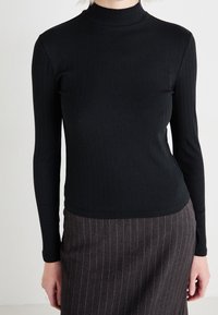 Svart ribbad polotröja med långa ärmar, som har en figurnära design. Tyget verkar slätt och elastiskt, vilket skapar en åtsittande silhuett.