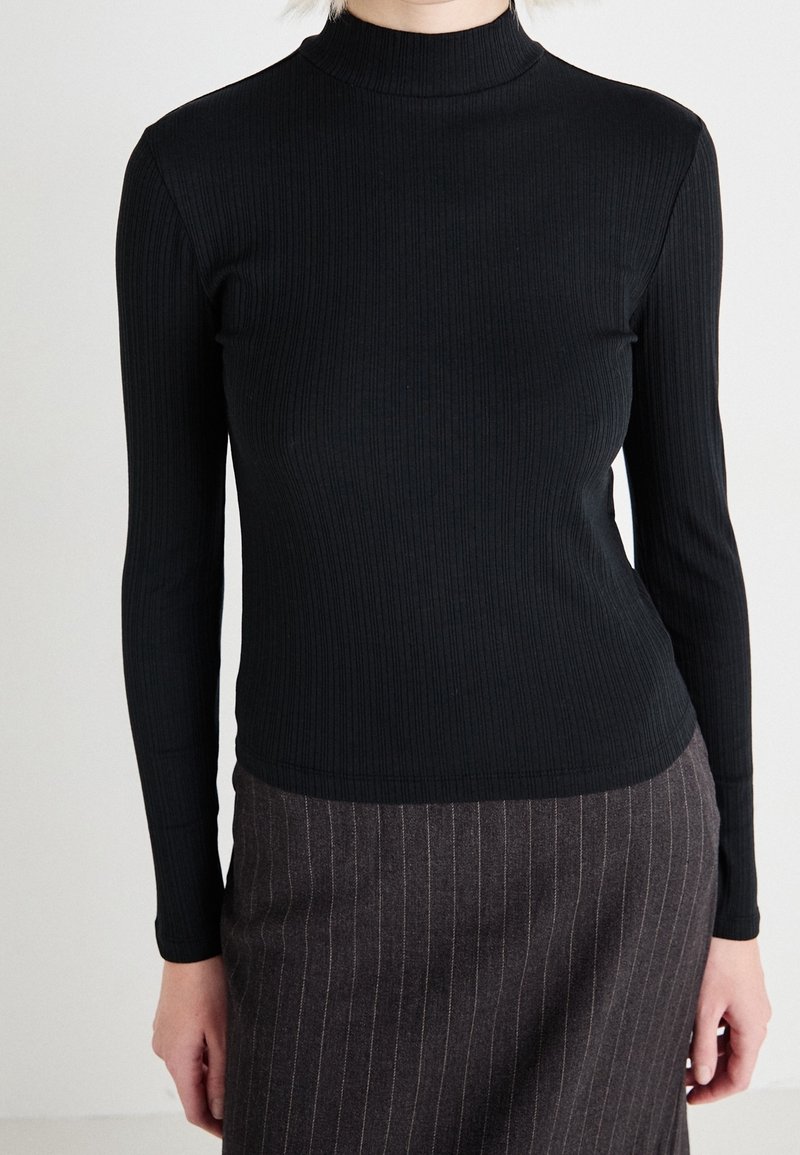 Svart ribbad polotröja med långa ärmar, som har en figurnära design. Tyget verkar slätt och elastiskt, vilket skapar en åtsittande silhuett.