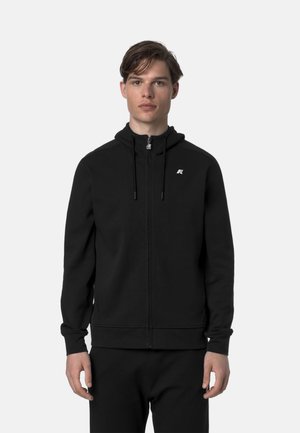 Felpa nera con zip realizzata in tessuto morbido, con un colletto alto, coulisse, tasche laterali e un piccolo logo sul petto.