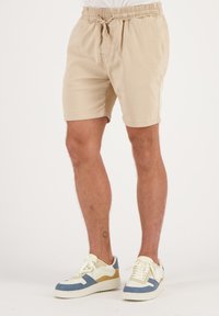 Beige shorts van lichtgewicht stof, met een elastische tailleband met een trekkoord en zijzakken. Draag ze met kleurrijke sneakers.