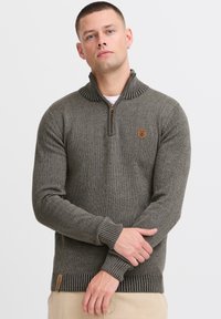 Brązowy sweter wykonany na drutach z zapięciem na kołnierzu, ściągaczami przy mankietach i u dołu, z małym emblematem na piersi oraz teksturowanym, ciepłym materiałem.