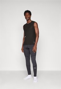 Top negru fără mâneci și pantaloni gri închis, ajustați, dintr-un material texturat, cu cusături de contrast, având un mic logo pe picior.
