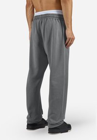 Pantaloni de trening gri cu talie elastică și căptușeală albă, având o croială lejeră și un textură netedă, purtați cu pantofi sport negri.