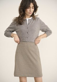 Cardigan gris avec des boutons, associé à une jupe à carreaux beige et marine. Le tissu semble doux avec un design ajusté.