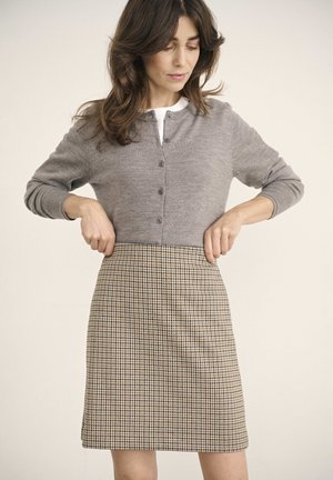 Cardigan gris avec des boutons, associé à une jupe à carreaux beige et marine. Le tissu semble doux avec un design ajusté.