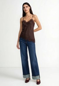 Rjava satenasta camisole z čipkasto obrobo, kombinirana s širokimi kavbojkami z zavihanimi hlačnicami in temno bordo čevlji.