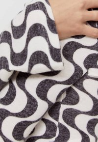 Hand auf einem Stoff mit auffälligem schwarz-weißen Wellenmuster ruhend, das die Textur und das abstrakte Design hervorhebt.