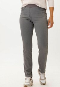 Pantalon gris ajusté avec une texture lisse, doté d'une taille confortable et de poches avant, associé à des chaussures de sport claires.