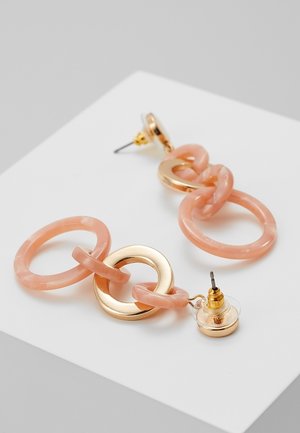 Boucles d’oreilles pendantes en anneaux liés rose et or avec attaches à tige, posées sur une surface blanche.