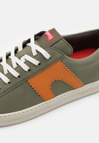 Olivgrön sneaker med orange detaljer, vita snören och gummisula. Har zickzack-söm och subtil logotyp på tungan.