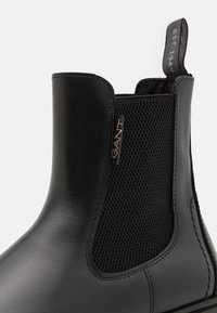Botte Chelsea en cuir noir avec panneaux latéraux élastiques et dessus texturé. Logo "GANT" doré et languette pour tirer. Finition lisse et détails cousus.