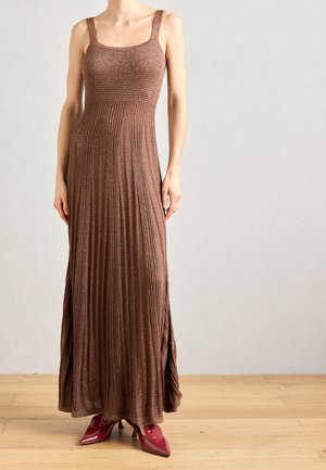 Robe longue en maille marron avec un corsage ajusté, un décolleté carré et une jupe plissée. Associée à des talons rouges à bouts pointus sur un sol en bois.