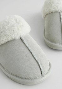 Gray suede slippers with a soft white faux fur cuff. Features a stitched seam and rounded shape. Smooth texture and flat sole design.