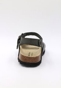 Sandale en cuir noir avec une semelle en liège, sangle réglable et surface texturée. Semelle en caoutchouc noir solide avec une forme arrondie.