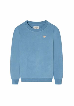 Niño con sudadera azul, pantalones cargo beige, zapatillas negras y gorra de béisbol amarilla, de pie y mirando hacia un lado sobre un fondo blanco.