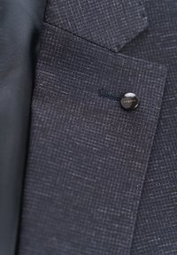 Dark blue textured fabric blazer featuring a subtle check pattern, with a black button and small contrasting stitching detail.