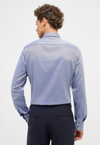 Lichtblauw overhemd met lange mouwen en een gestructureerd, ruitenpatroon; voorzien van contrasterende donkerblauwe accenten op de schouders en manchetten.
