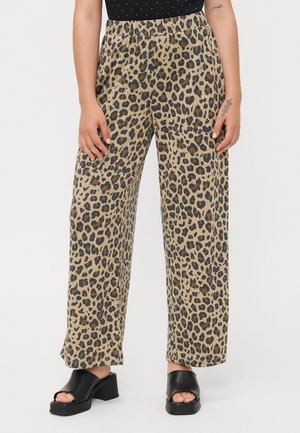 Weit geschnittene Leopardenmuster-Hose mit elastischem Bund, getragen mit schwarzen Sandalen mit offenem Zehenbereich und Blockabsatz, an einer stehenden Person.