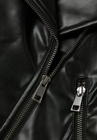 Primo piano di due cerniere d'argento su tessuto in pelle nera texturizzata, con cuciture dettagliate e denti della cerniera leggermente aperti.