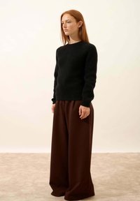 Schwarzer, strukturierten Strickpullover kombiniert mit lockeren, weiten, braunen Hosen. Das Outfit hat ein einfaches, modernes Design mit einem entspannten Sitz.