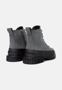 Sneaker alte grigie con suola testurizzata, dotate di una cerniera laterale e lacci, presentate da un'angolazione posteriore su uno sfondo chiaro.
