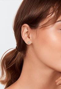 Pendiente de plata en forma de corazón en un modelo. Superficie lisa, tamaño pequeño, situado en el lóbulo, con un diseño minimalista.