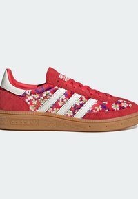 Rote Wildleder-Sneaker mit weißen Streifen, floraler Stickerei und einer Gummisohle in Kautschuk-Optik. Details beinhalten einen gepolsterten Schaft und ein Markenetikett auf der Zunge.