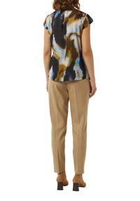 Kurzärmlige Bluse in blau, schwarz und braunem abstraktem Muster; glattes Material; kombiniert mit beigen, taillierten Hosen und Schuhen mit Blockabsatz.