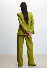 Traje verde lima a medida con un blazer estructurado y pantalones de pierna ancha, que presenta una textura suave y costuras alineadas, visto desde la parte de atrás.
