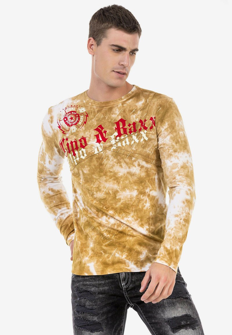 Langärmliges T-Shirt mit Batikmuster in Braun und Beige, das rote und weiße Schriftzüge aufweist. Der Stoff hat eine weiche, strukturierte Optik mit einem runden Ausschnitt.