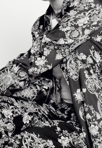 Czarno-biały kwiecisty wzór na ubraniu wykonanym z jedwabistej tkaniny, z misternymi motywami kwiatów i elementów dekoracyjnych.