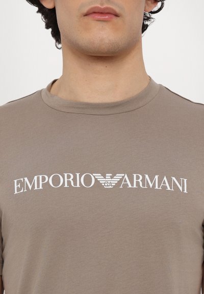 Brown cotton t-shirt featuring a crew neck and short sleeves, with a prominent white "Emporio Armani" logo printed across the chest.