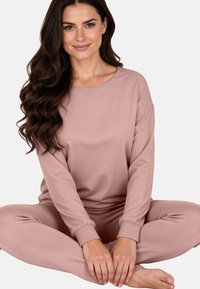 Világos rózsaszín szabadidőruha készlet lazább szabású, hosszú ujjú felsőből és elasztikus szegélyű nadrágból áll. Puha anyag és sima textúra, kényelemre tervezve.
