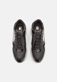Sneaker in pelle nera con dettagli in vernice, punta rotonda e inserti in rete. Presenta lacci neri e branding stampato sulla linguetta.