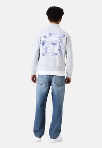 Sudadera gris con un estampado gráfico en la parte posterior, combinada con jeans de pierna ancha de color azul claro y zapatillas blancas. Ajuste casual, material de algodón.