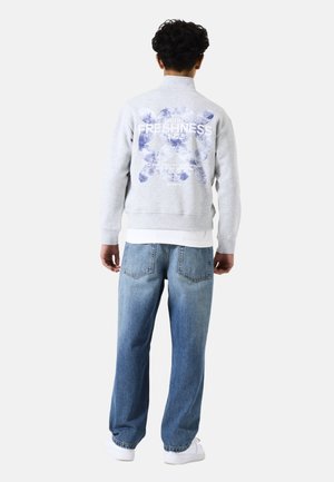 Sudadera gris con un estampado gráfico en la parte posterior, combinada con jeans de pierna ancha de color azul claro y zapatillas blancas. Ajuste casual, material de algodón.