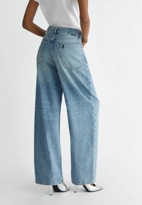 Light blue wide-leg jeans made of denim with a high waist, two back pockets, and a raw hem, paired with silver heeled shoes.